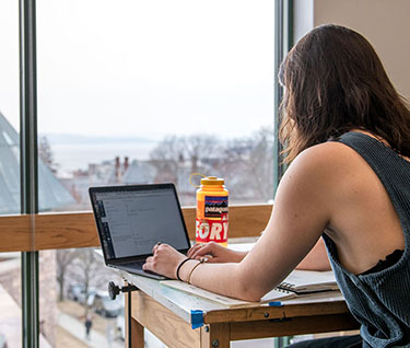 Champlain College student working on a laptop in front of big window