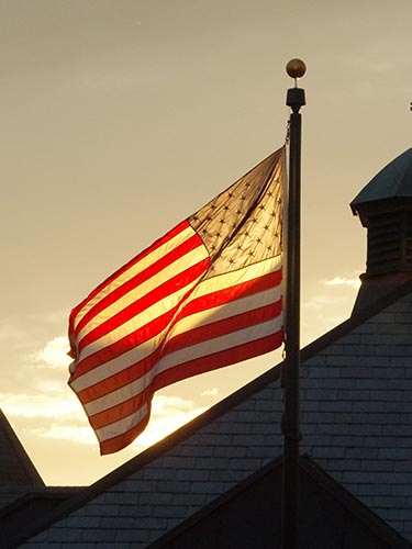 An American flag flies over campus with sunset backlight
