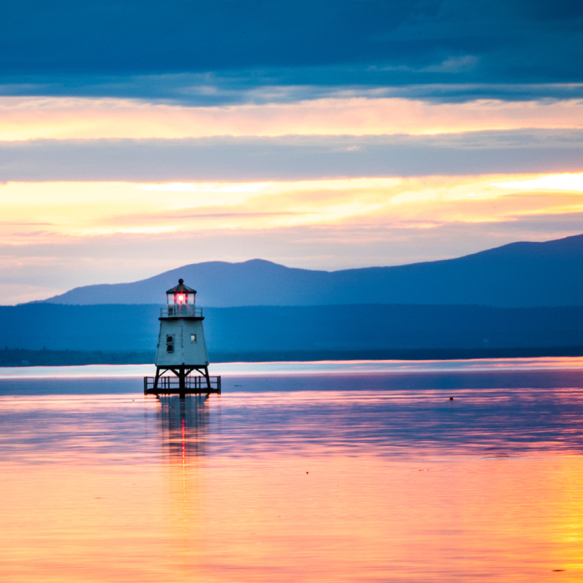 Sunset view of a lighthouse on Lake Champlain and mountains in the distance