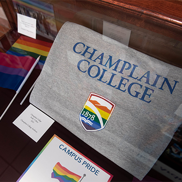 Display case including multiple kinds of pride flags a sign that reads campus pride and a Champlain College tshity with the college's shield in rainbow colors