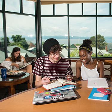 Three students studying in the library's Vista Room with Lake Champlain and the Adirondack Mountains visible through the windows
