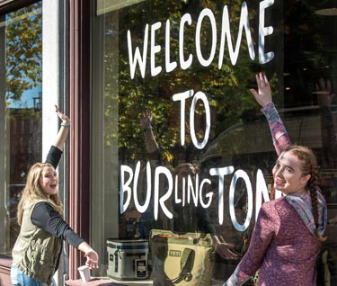 Two students posing in front of a store window that says "Welcome to Burlington"