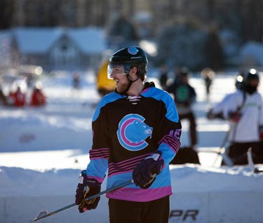 Student hockey player dressed in hockey gear posing with a hockey stick outside on a frozen Lake Champlain