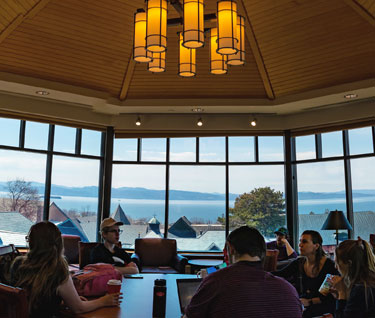 Students collaborate in a study group in the top floor of the library with a view of campus and Lake Champlain in the background.