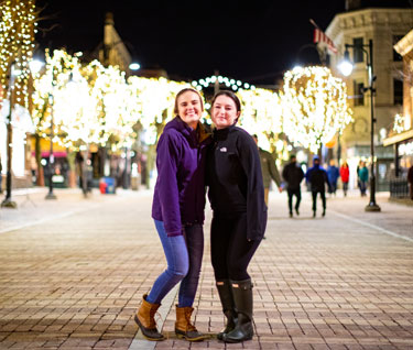 Two students stand on Church Street with holiday lights behind them.