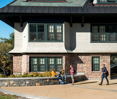 Close up shot of the front of Lakeview, a contemporary res hall, with students standing outside the building.