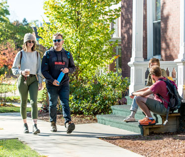 Two students walk towards two other friends who are sitting on the steps of a residence hall