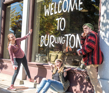 Three students pose in front of Burton's flagship store with "Welcome to Burlington" written on the window.