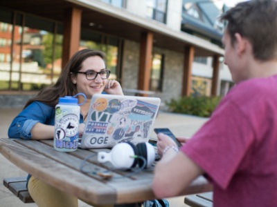 Two Champlain College students sitting with a laptop outside on of the Champlain College residence halls.