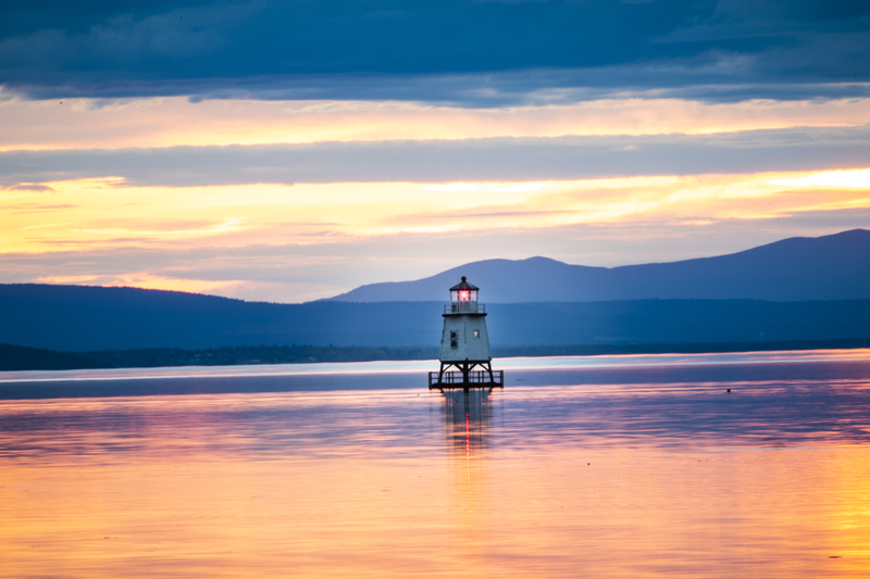 A light house in Lake Champlain as the sun sets over the Adirondacks.