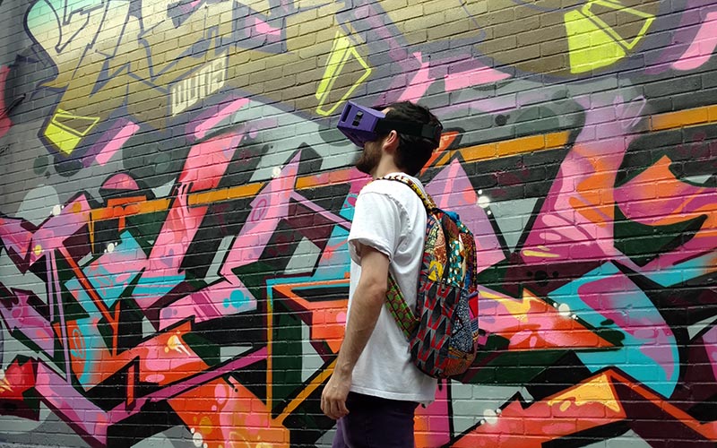 Champlain student wearing VR headset walks past a wall of street art