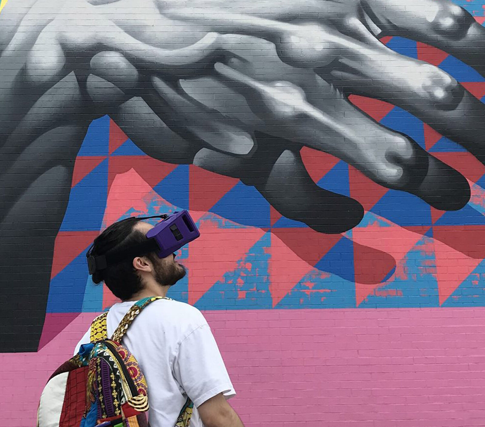 A student wearing what appears to be a VR headset looking towards a mural on a wall of a gray hand over a colorful background.