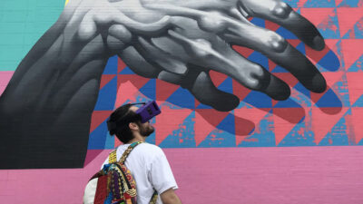 A student wearing what appears to be a VR headset looking towards a mural on a wall of a gray hand over a colorful background.