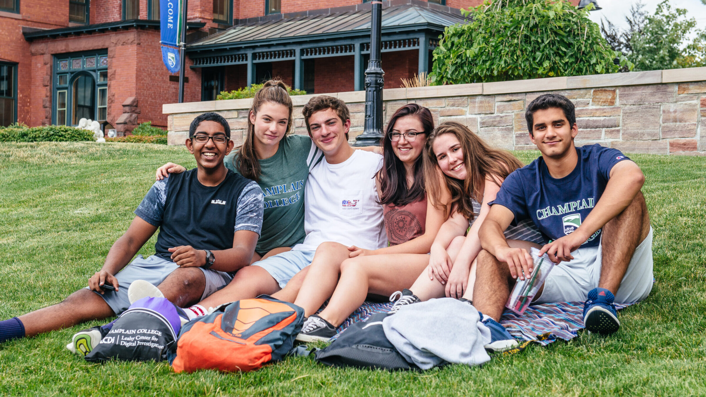 group of students sit on a blanket on the lawn