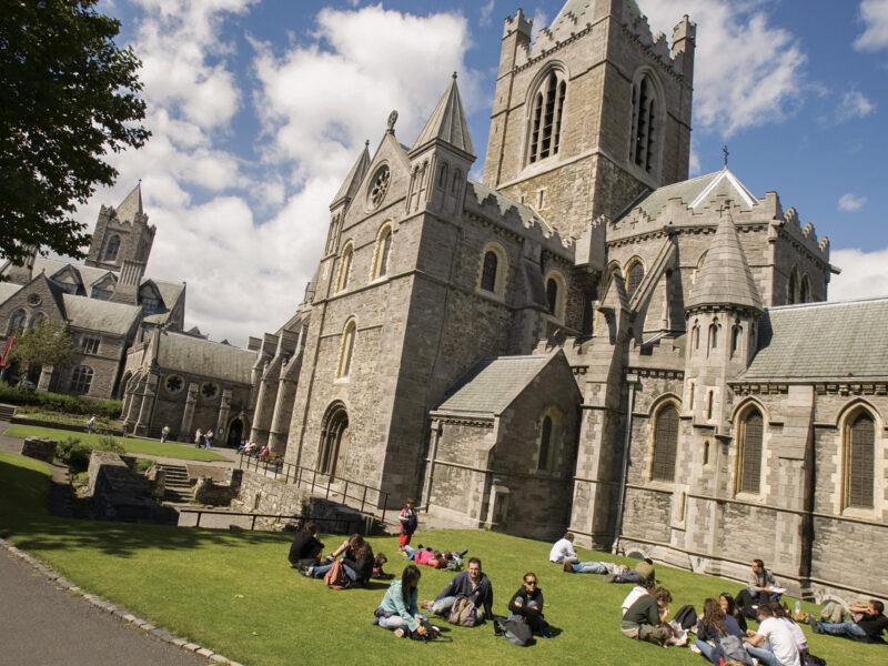 people sitting on the lawn of a church-like building in Dublin enjoying the sunny day