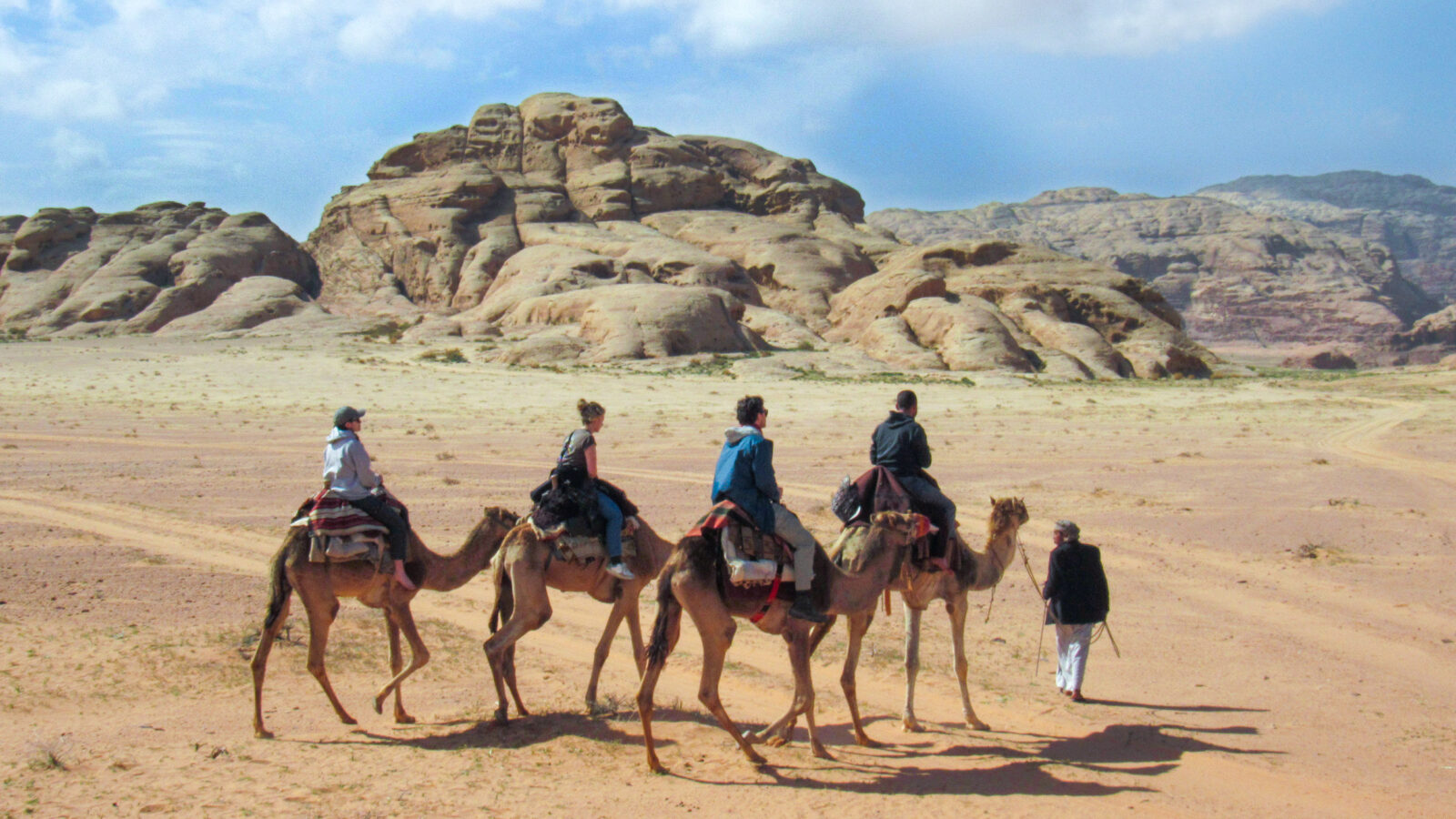 small group of people ride camels across the sandy desert