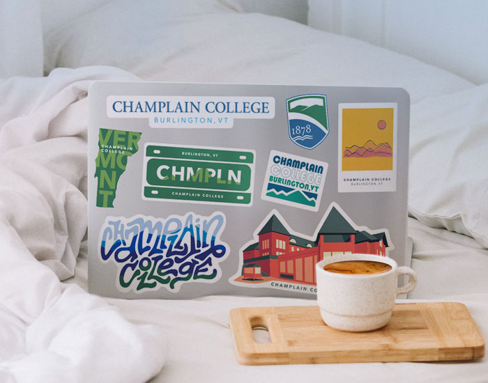 Laptop on a bed, the laptop is decorated with exciting stickers from a champlain college graduate
