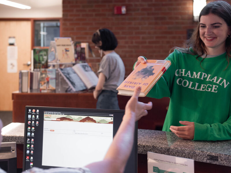 A student hands a book to an employee behind a desk to check out from the library