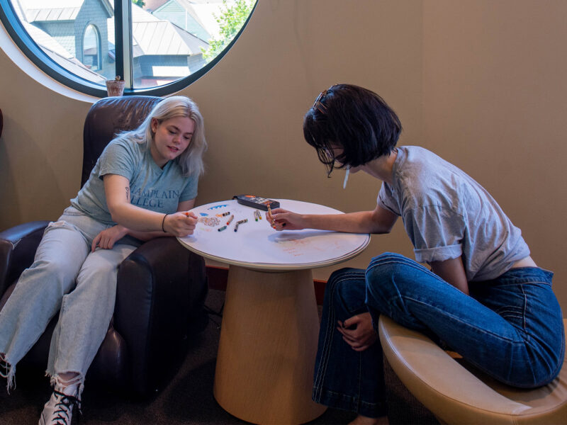 Two students coloring on a paper table in the second floor tower room of the library