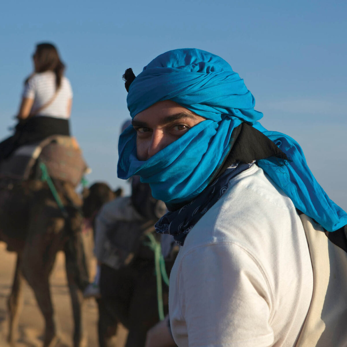 an abroad student in morocco, wearing a head covering while walking with camels in the desert