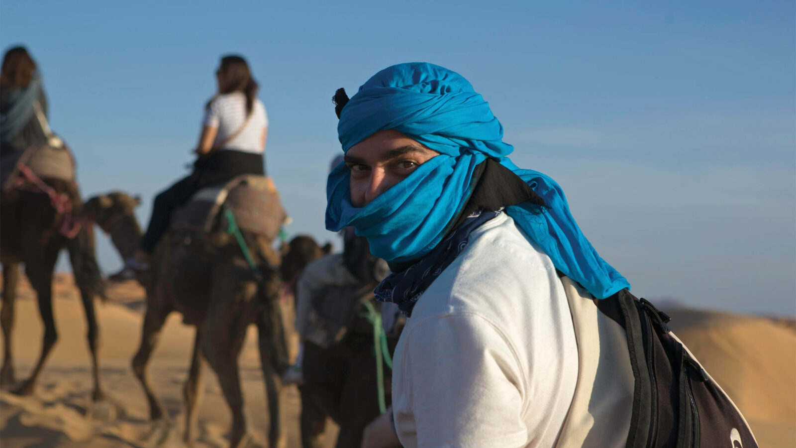 an abroad student in morocco, wearing a head covering while walking with camels in the desert