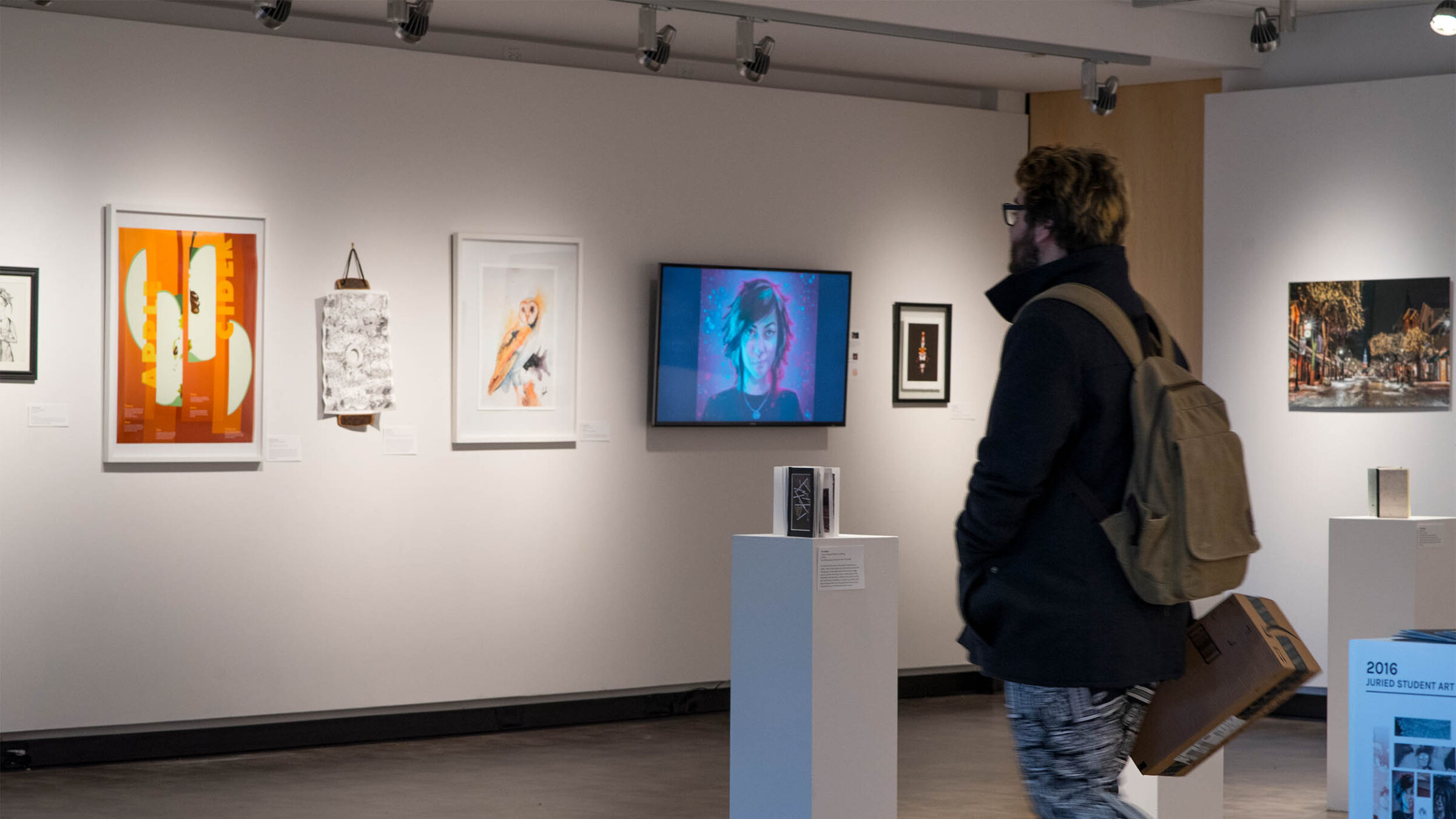 man looks at artwork displayed on a gallery wall