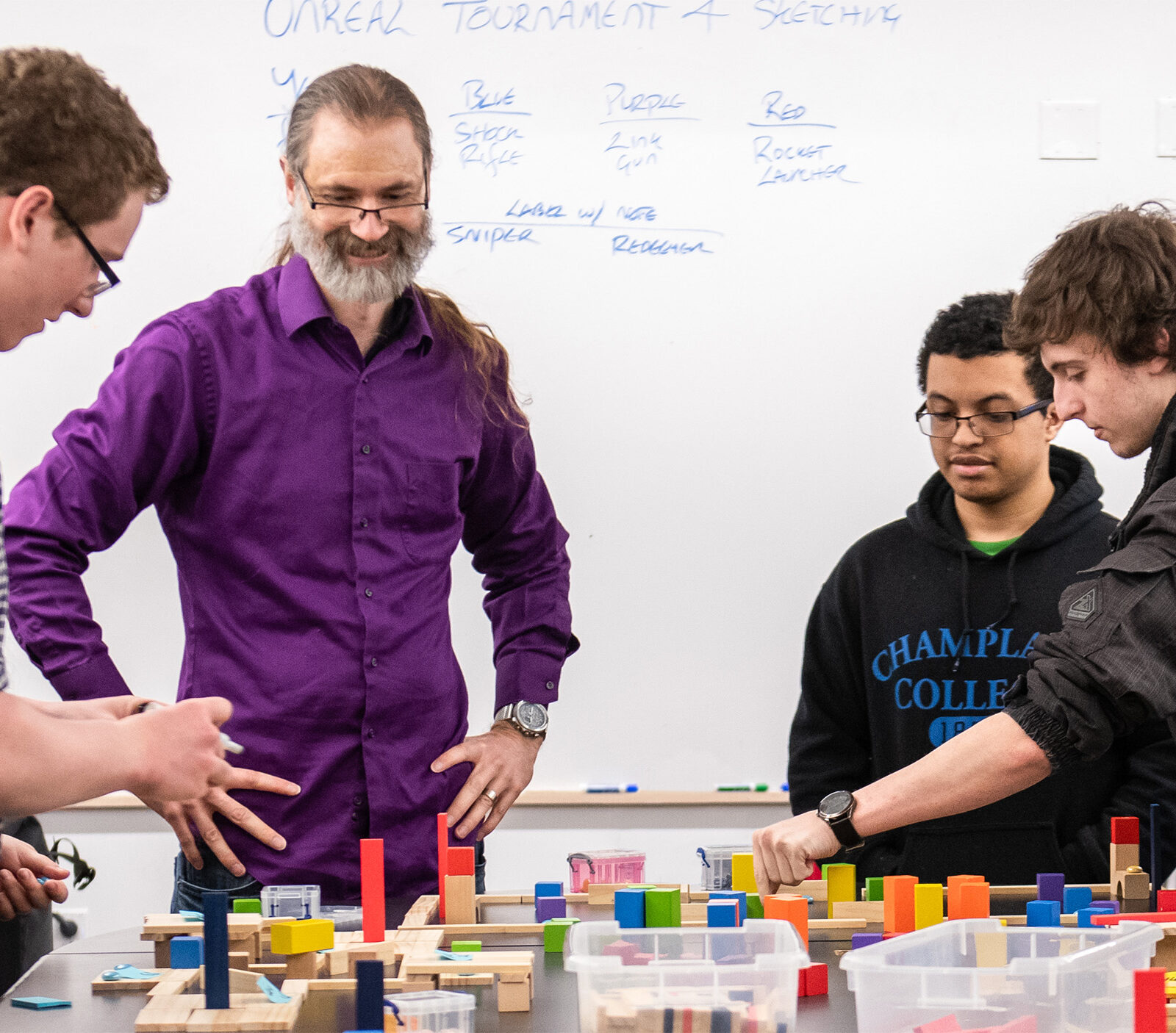 Teacher and students discussing game design and strategy with block props on a table.