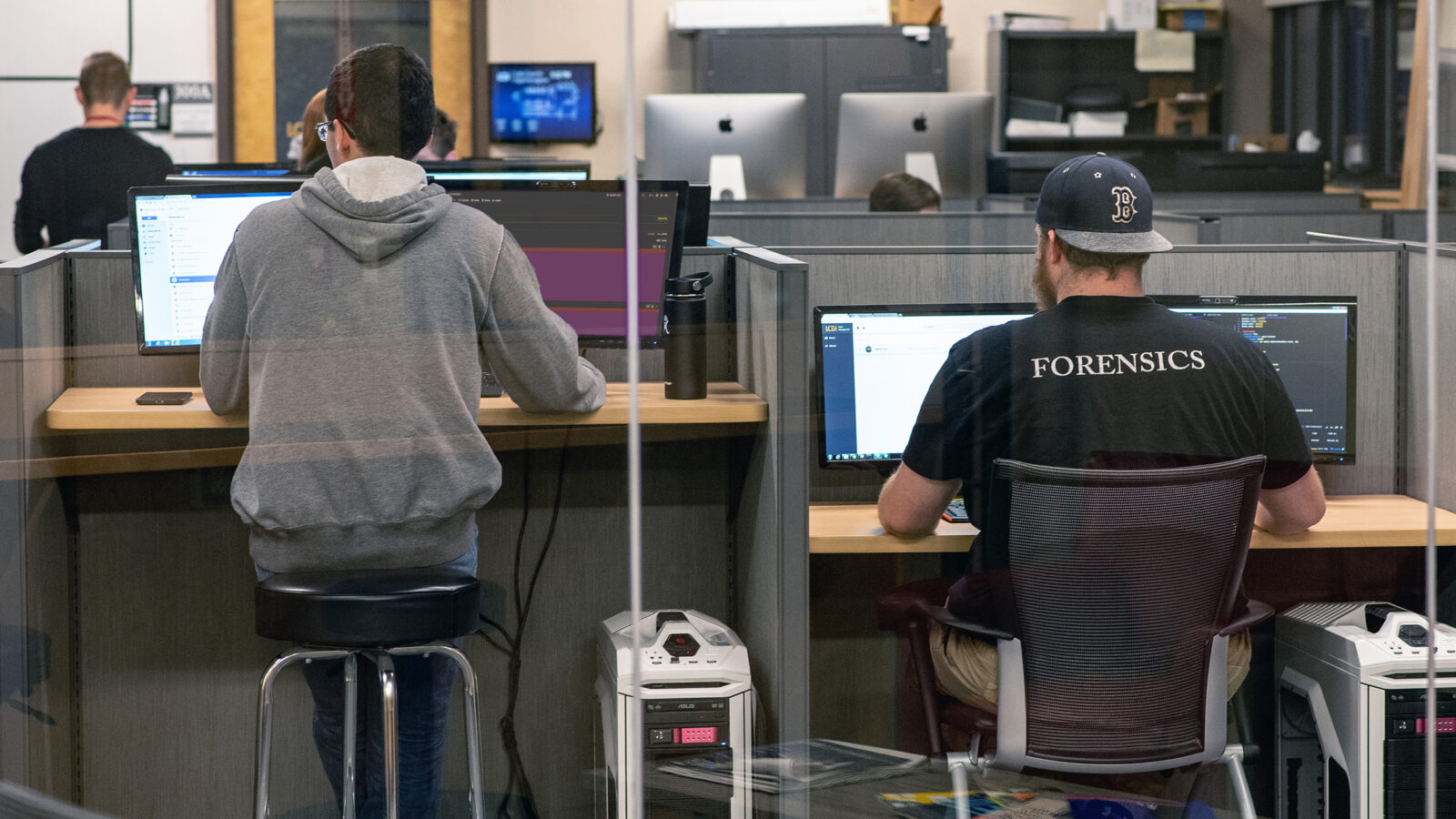 students facing computers; "forensics" on the back of student t-shirt
