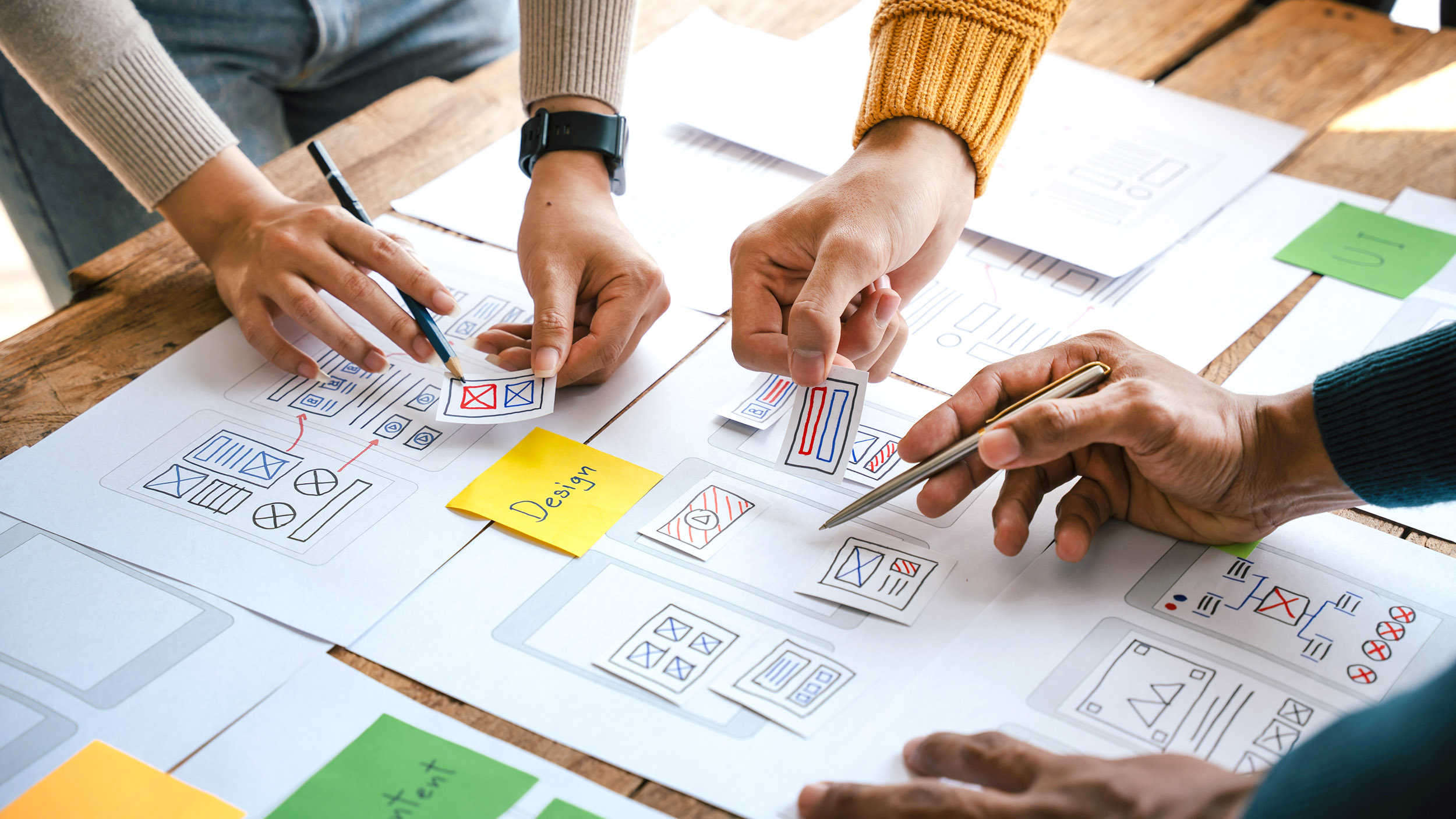 three people working together to come up with a UX/UI design on a table with papers and pens