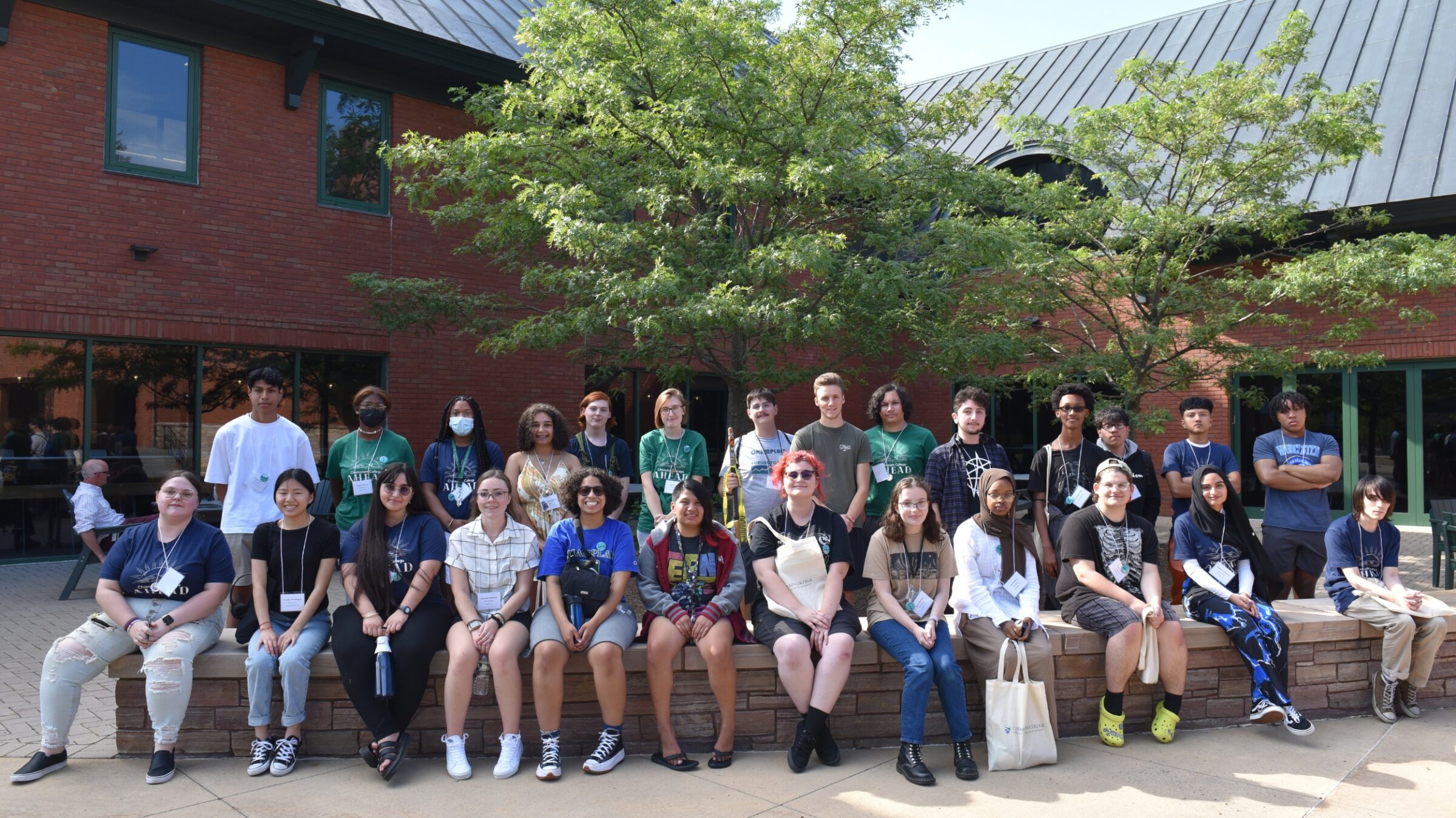 students sit and stand smiling at the camera for a group photo in the sunny courtyard