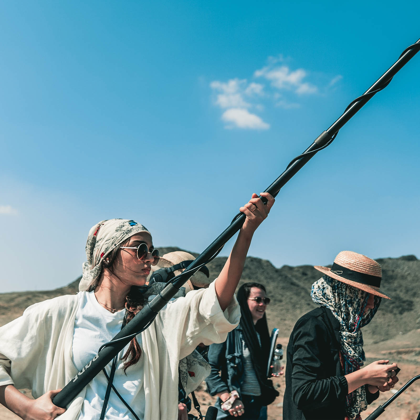 a small group of filmmaking students working on a production in the desert, with one holding a boom microphone and another operating the camera