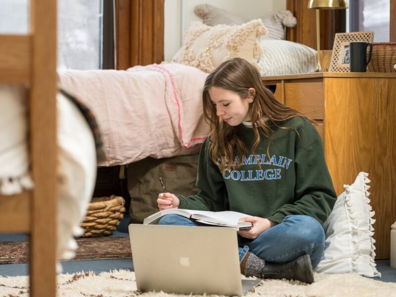 Student sitting on the dorm floor working in a notebook and laptop