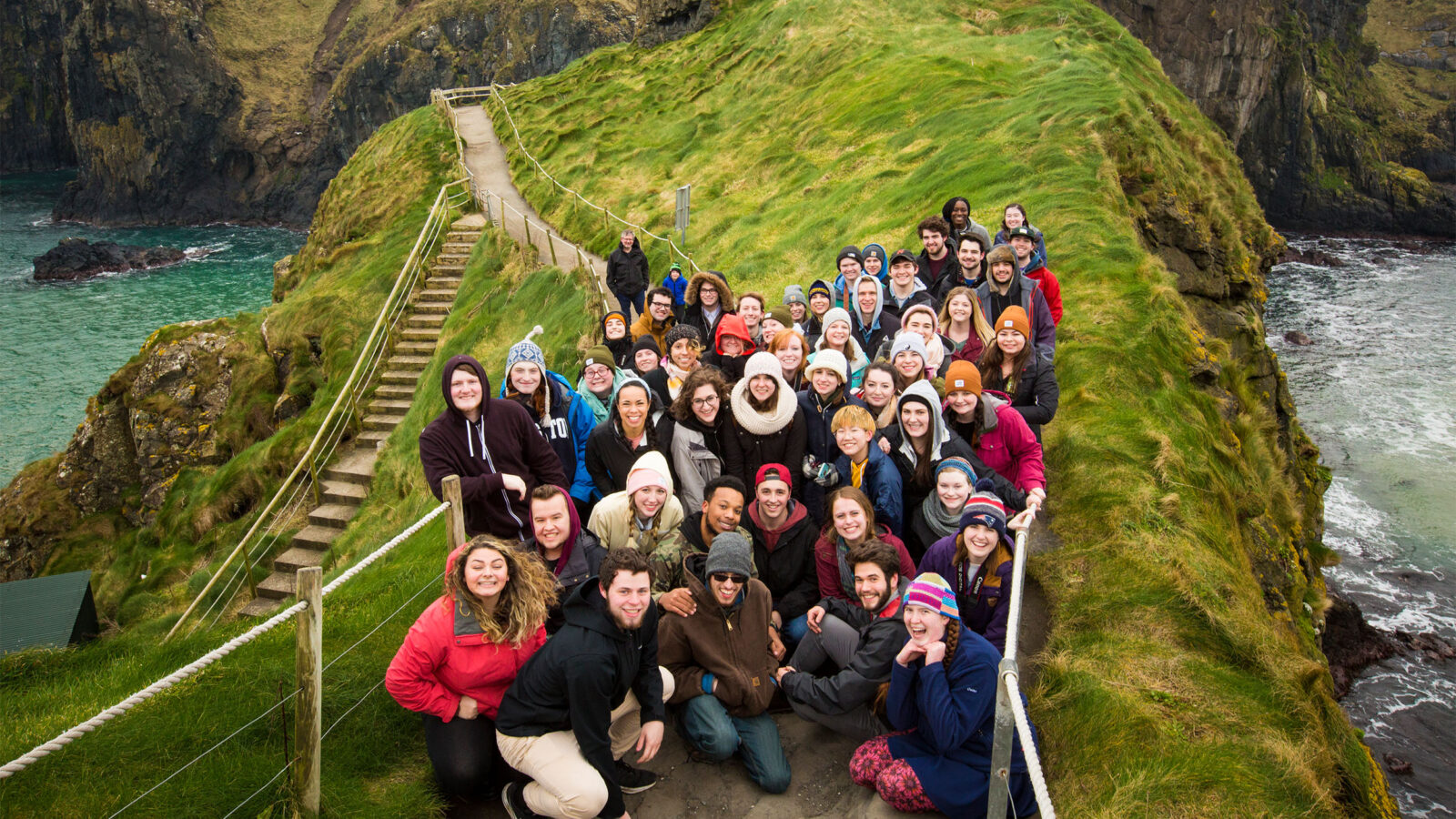a large group of abroad students gather for a group photo on the cliffs of northern ireland