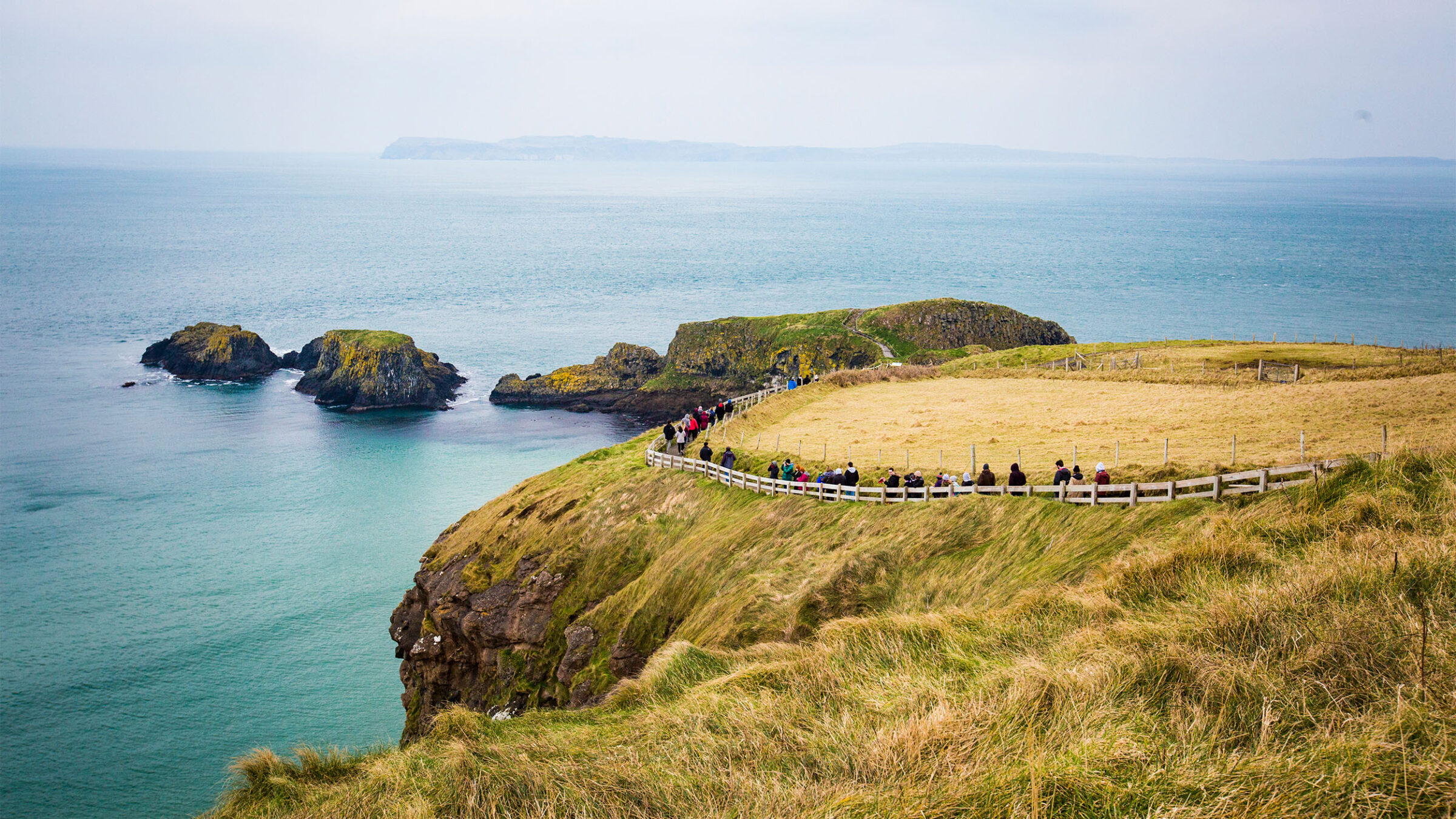 a group of students and tourists walking a path along a cliff side in northern ireland