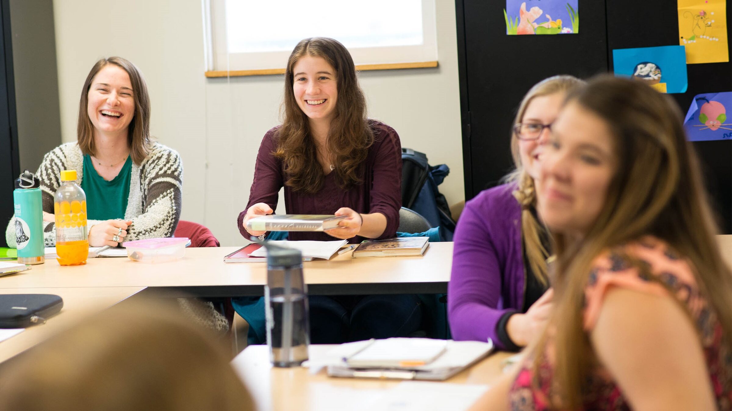 education students sit at desks, having a discussion, laughing