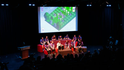 a team of game studio students presenting their game project to a full audience in an auditorium