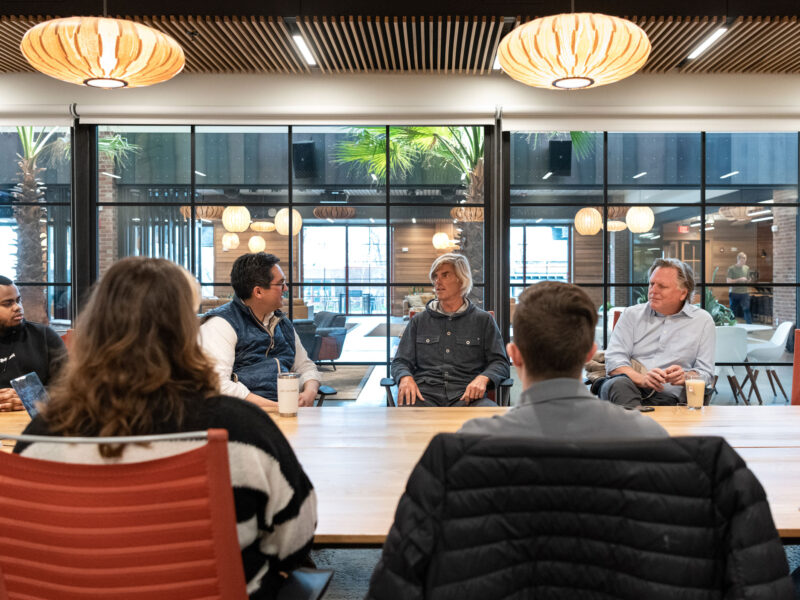 Champlain students sit around a table in a glass room listening to guest speakers at Hula, the business incubator space.