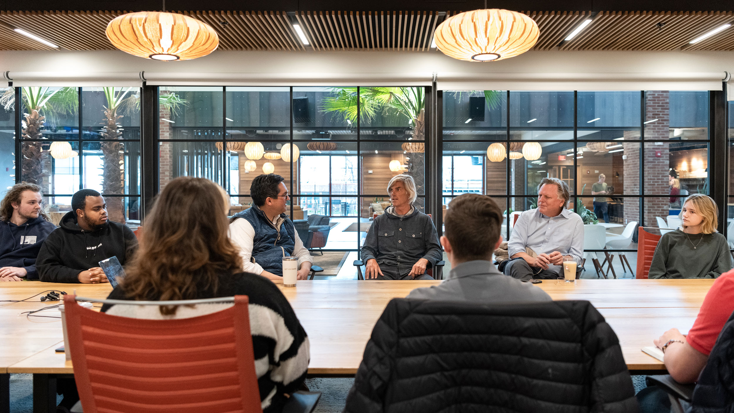 Champlain students sit around a table in a glass room listening to guest speakers at Hula, the business incubator space.