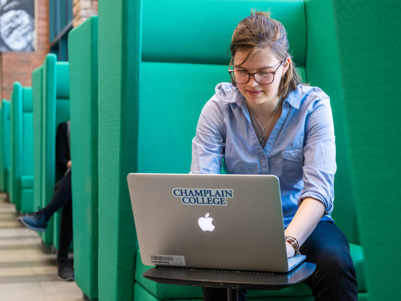 A student in CCM working on their laptop in a green chair