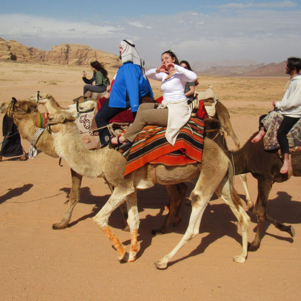 abroad students riding camels through the desert of jordan while waving at the camera