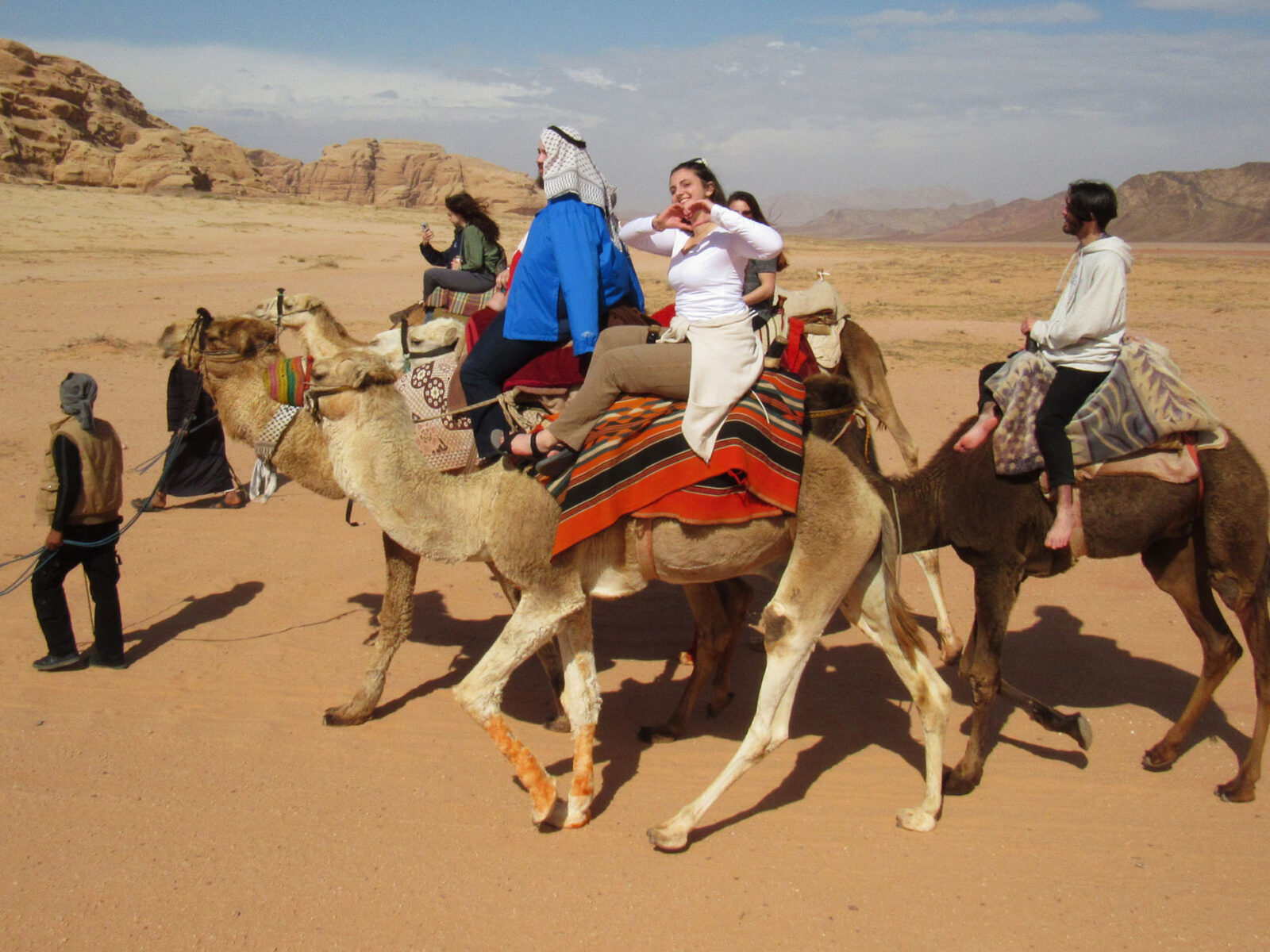 abroad students riding camels through the desert of jordan while waving at the camera