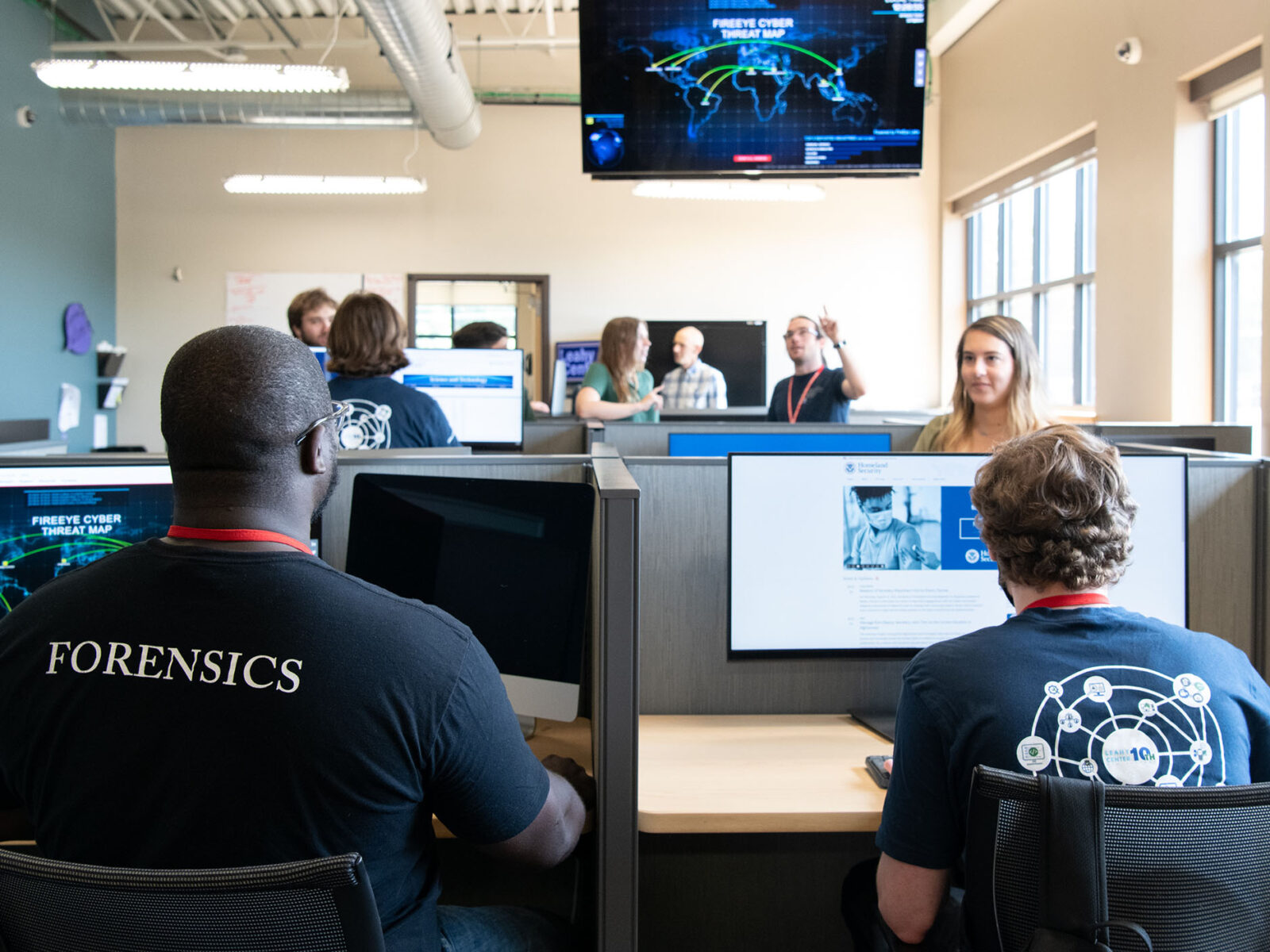 Two digital forensics students in a room of other students working on projects