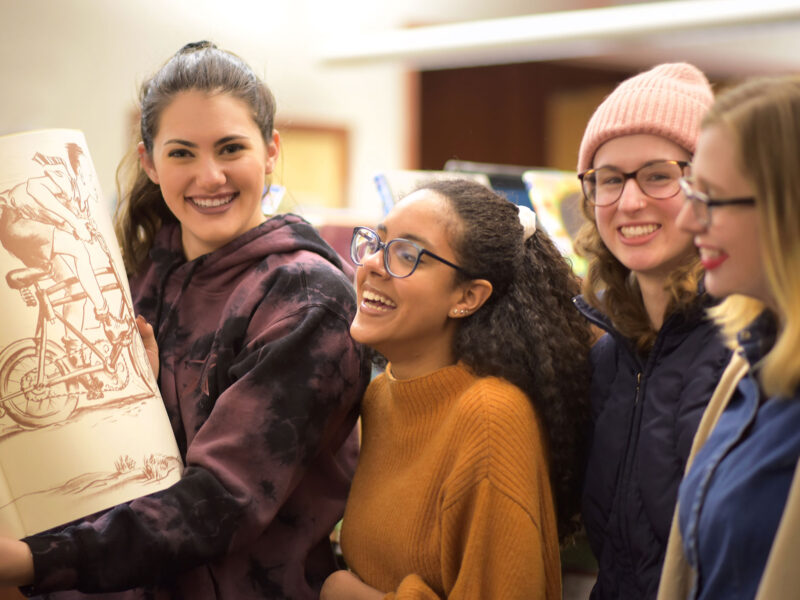 Four students look at an illustration book in the library