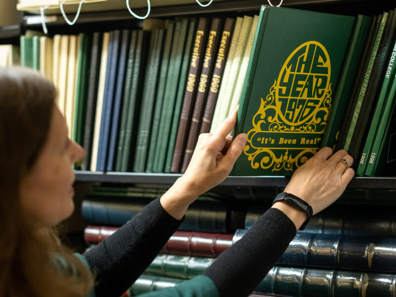 An employee removes the 1976 Champlain College yearbook from a shelf of yearbooks and other historic books