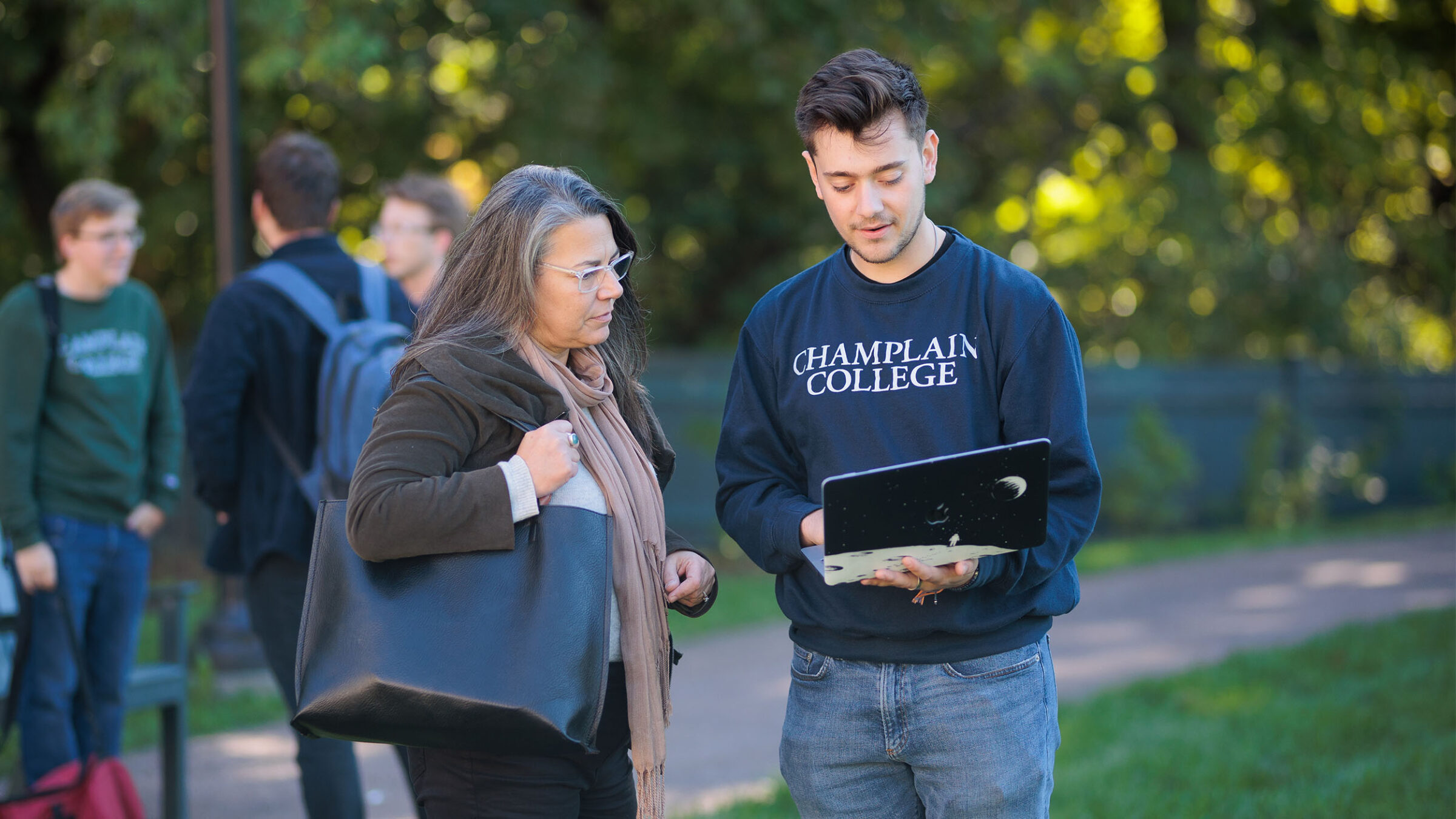 student showing a professor something on their laptop outside between classes