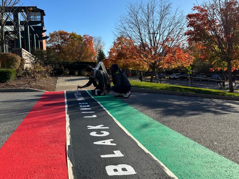 two people repaint the red, black, and green crosswalk on campus that says "black lives matter"