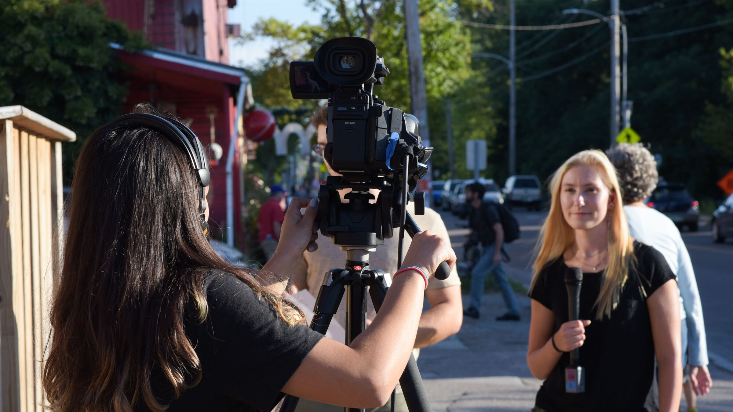 A broadcast student with a camera and another in front of the camera with a mic are working on a project