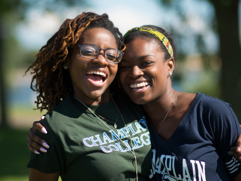Two female students in Champlain shirts hugging each other and smiling at the camera.