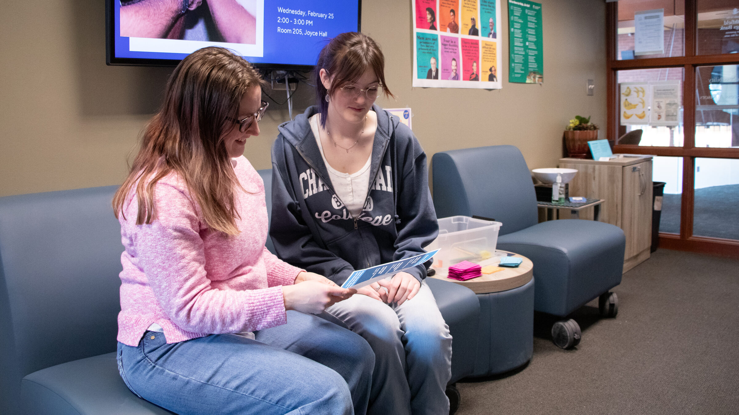 An advisor in a pink sweater reviews a brochure with a Champlain College student seated together in a Student Success Center lounge area.