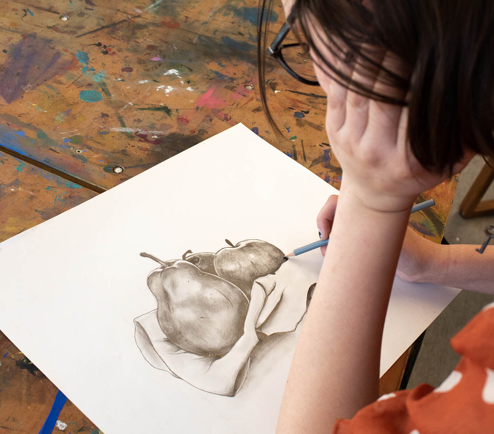 student works on a pencil drawing of a pear and apple